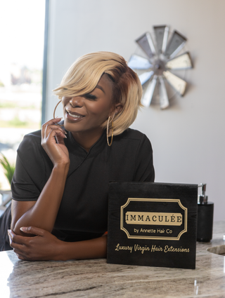 Woman in ombré warm brown to blonde, short Bob wig playing with hoop earring, smiling.