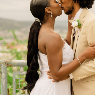 Bride wearing sleek waist length long ponytail with soft curls and an embellished ponytail wrap at the nape. Sweetly kissing groom. 